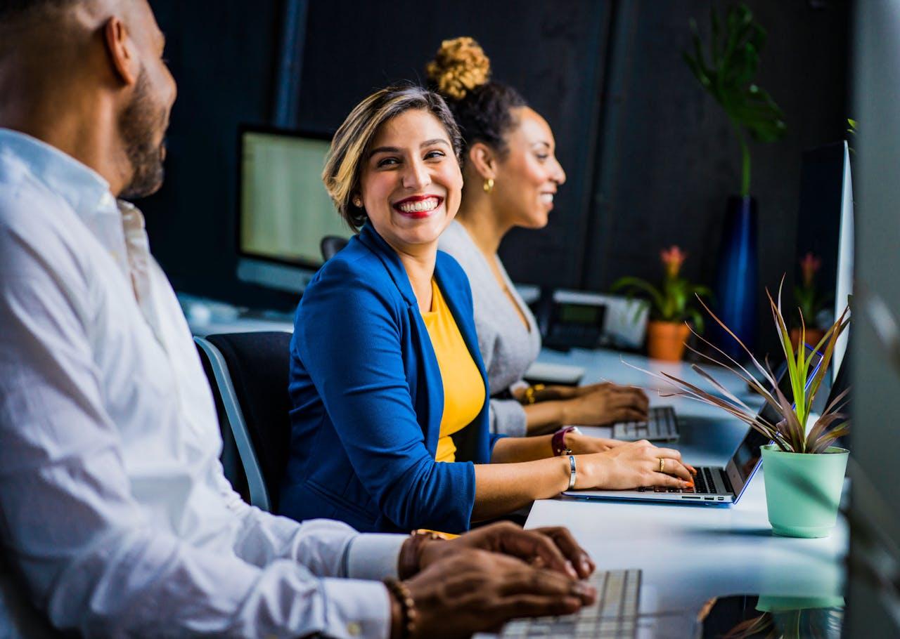a group of people working at a desk all smiling.