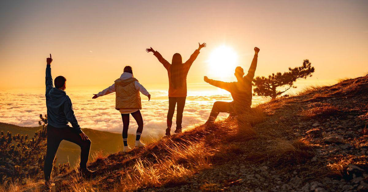 four people celebrating on a hill while the sun is setting.