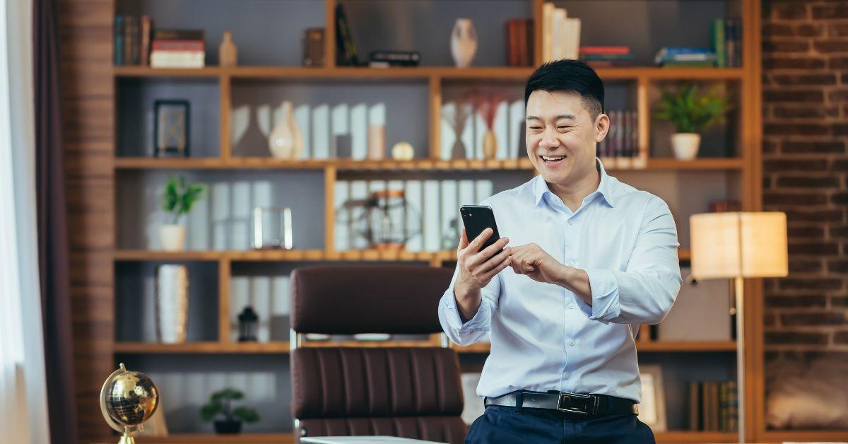 guy on his phone smiling while standing in a study room.