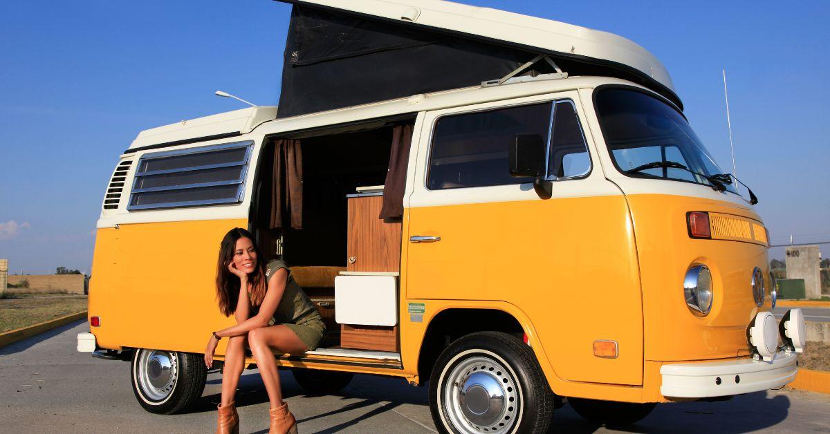 A yellow RV with the side door open and a woman sitting on the edge of it.