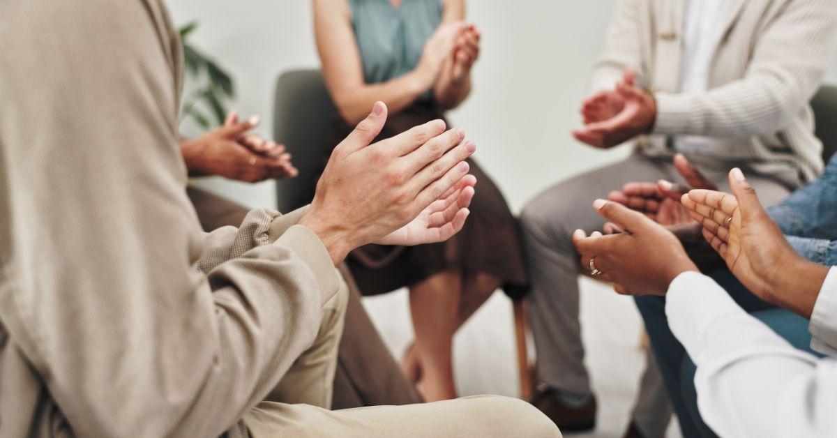 A group of people sitting in a circle clapping their hands.
